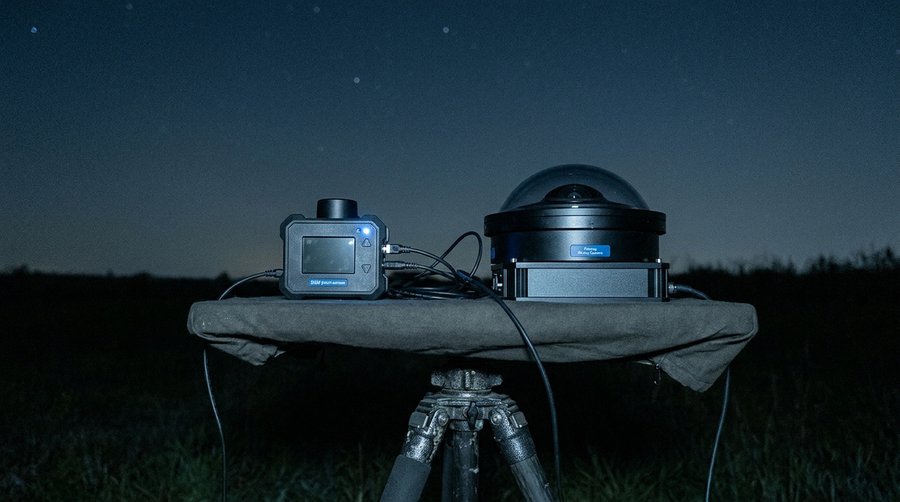 SQM point-sensor and fisheye all-sky camera side by side on a measurement table under a dark night sky