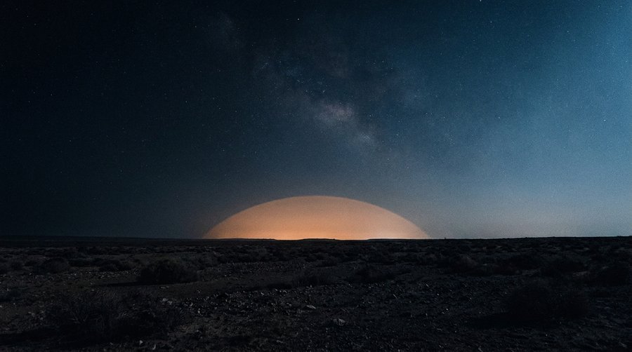 City light dome visible as an orange hemisphere on the horizon seen from flat dark terrain 50 km away