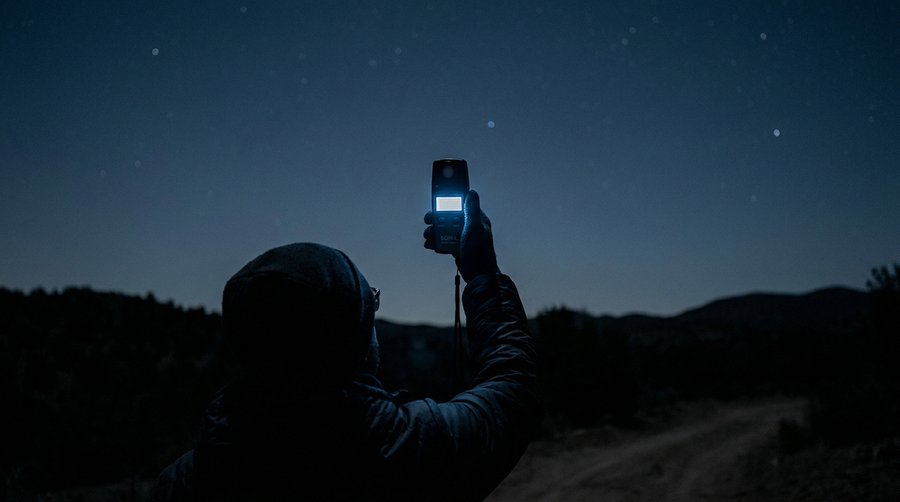 Person holding an SQM device at zenith against a clear starry sky demonstrating correct measurement technique